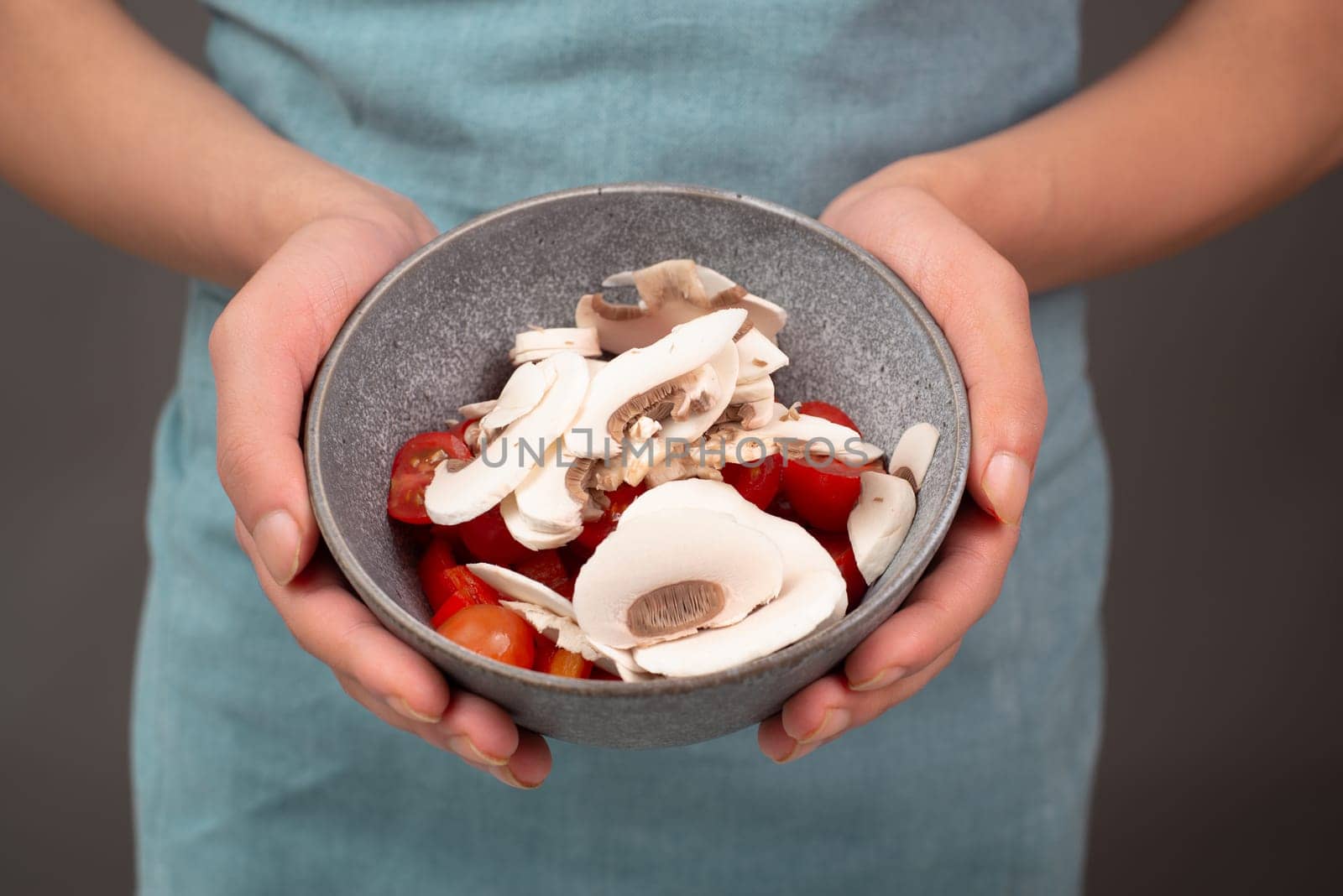 Sliced mushroom and tomato pieces in a salad bowl, prepare healthy food with vegetables, holding fresh organic nutrition in the hands