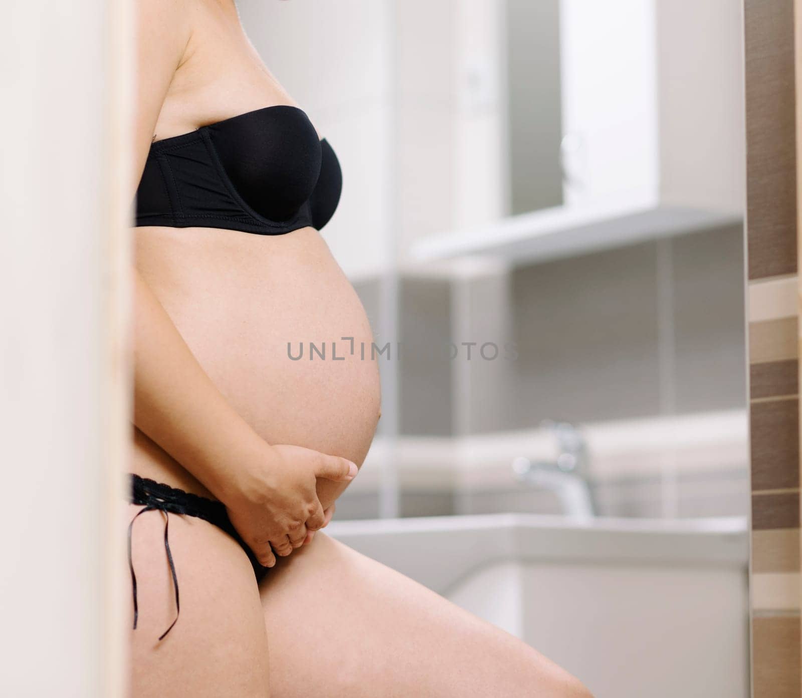 Pregnancy skin care for stretch marks. Beautiful pregnant woman in bathroom. Maternity cosmetics and skincare products.