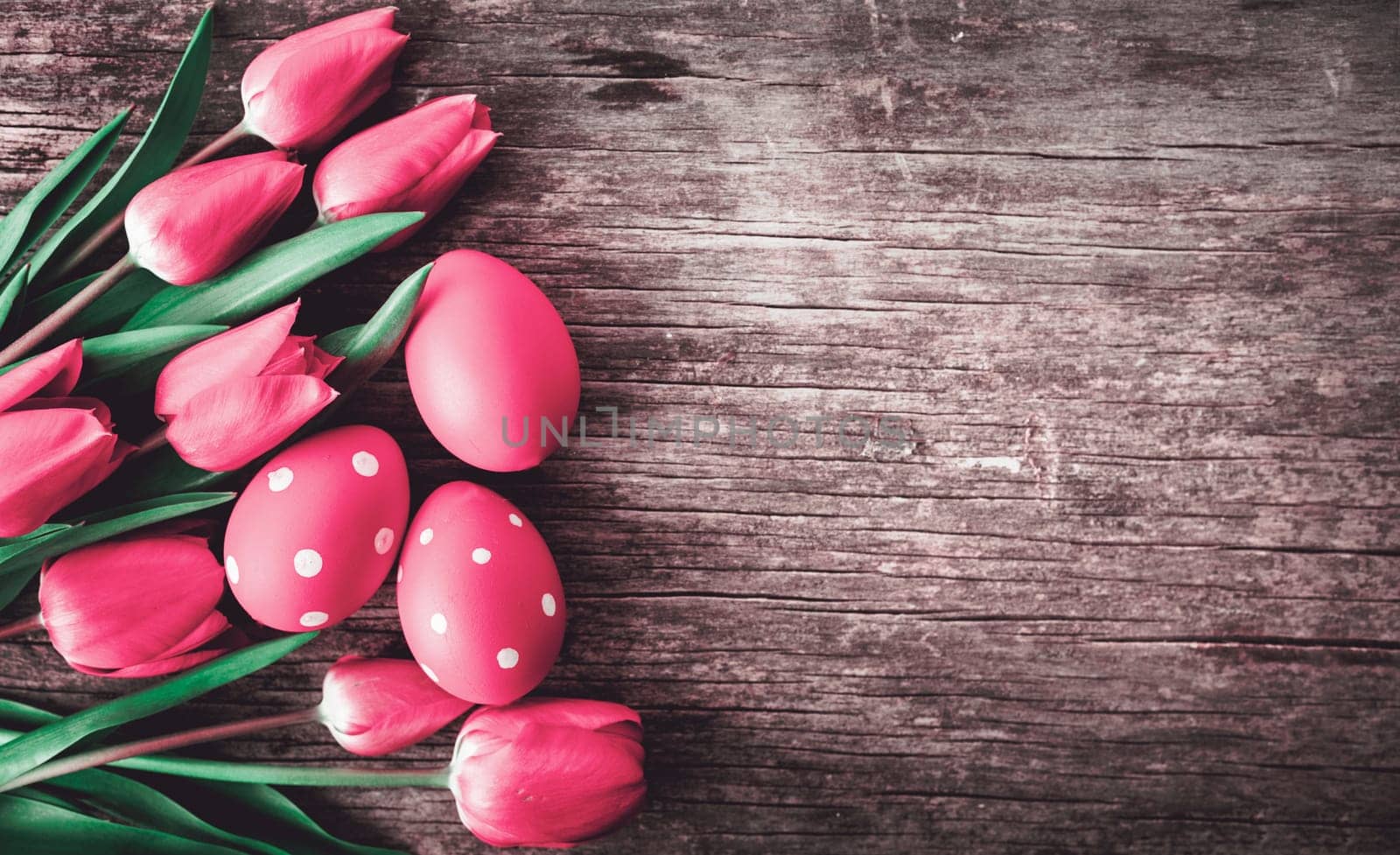 Red easter eggs and pink tulip flower on vintage wooden table from above. Easter holiday and springtime background design. Top view.