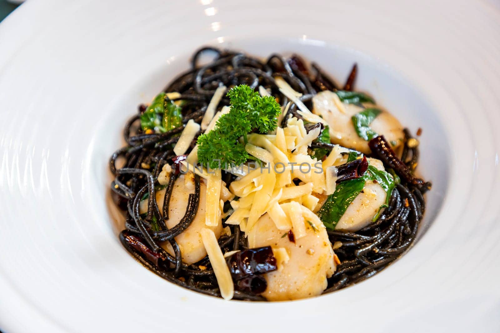 Spaghetti with scallops and sprinkled with cheese in a white plate. The black spaghetti has a slightly salty and spicy taste. Scallops are sweet and nutty. The cheese is salty and oily, so it's mellow