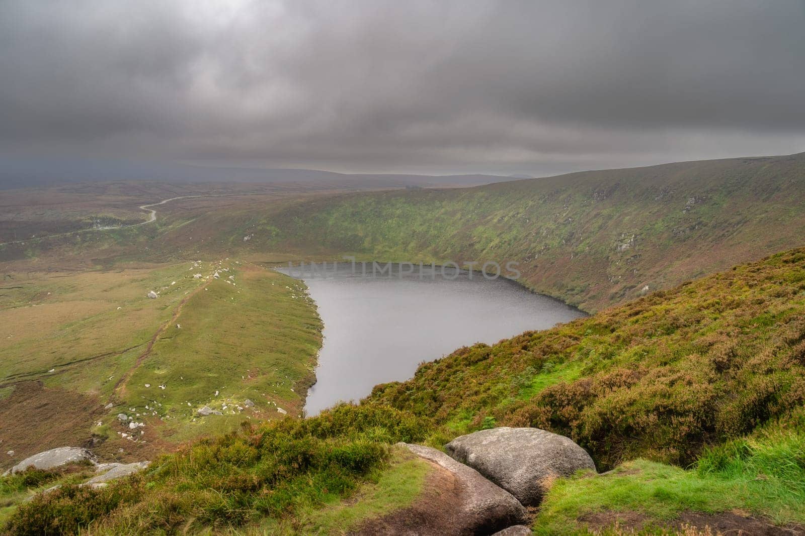 View on the lake Lough Bray from the top of the hill, covered in moody, dramatic storm clouds. Hiking in Wicklow Mountains, Ireland