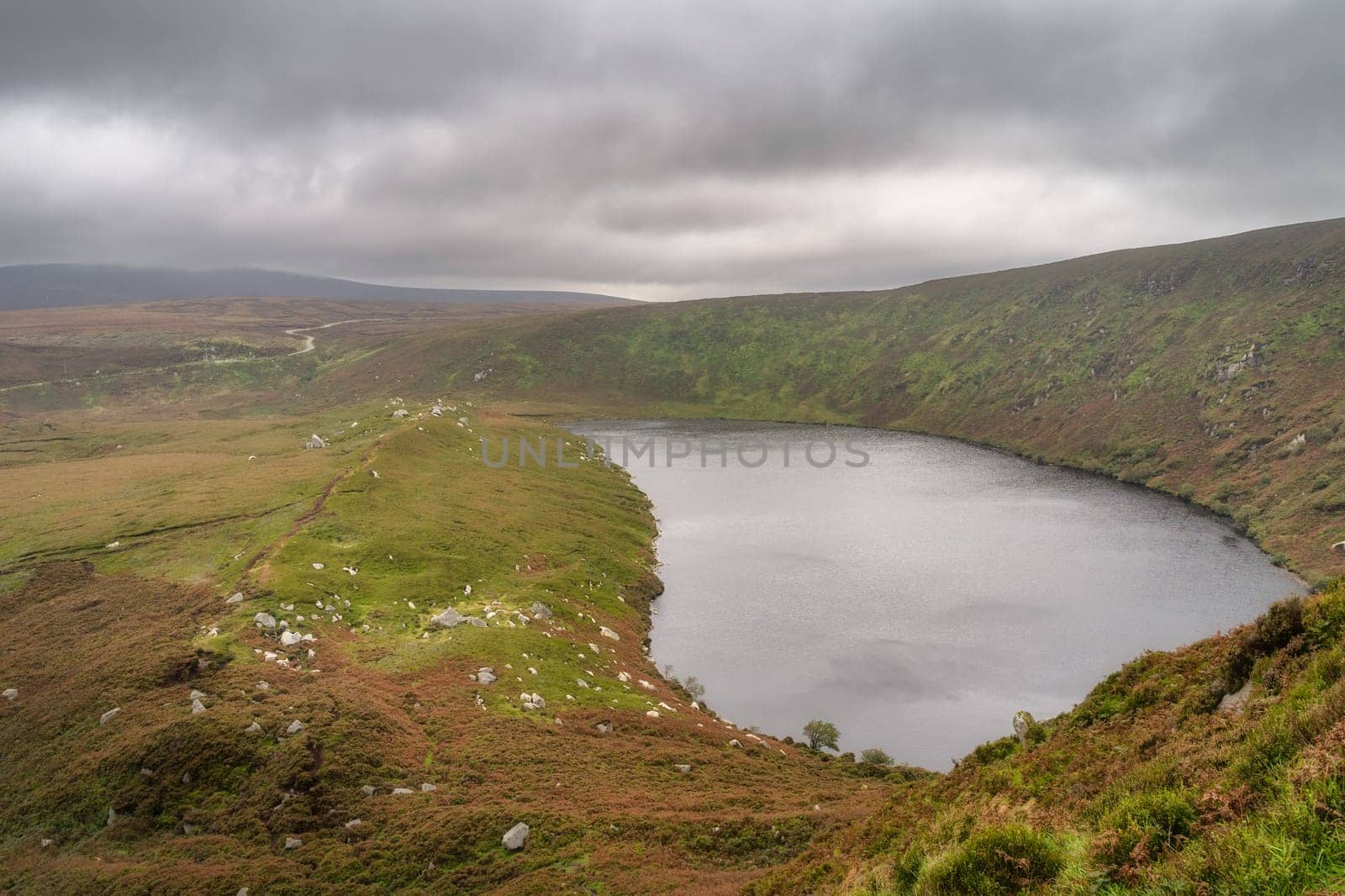 Lake, Lough Bray with mountain trail on the left and cliffs on right, covered in moody, dramatic storm clouds. Hiking in Wicklow Mountains, Ireland