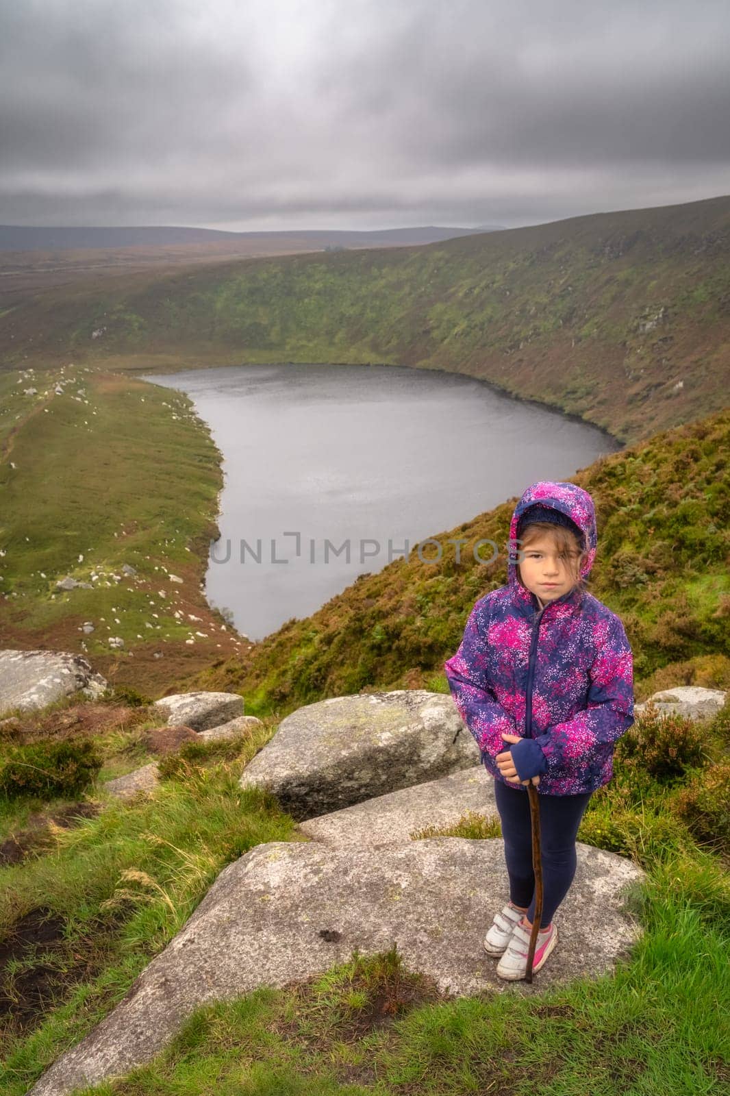 Young girl standing on the rock on the top of the mountain with lake, Lough Bray, down in background. Family hiking in Wicklow Mountains, Ireland