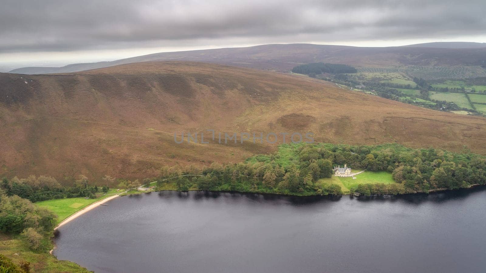 Mansion or house and beach hiding in small forest at the edge of lake Lough Bray, surrounded by dramatic storm clouds. Wicklow Mountains, Ireland