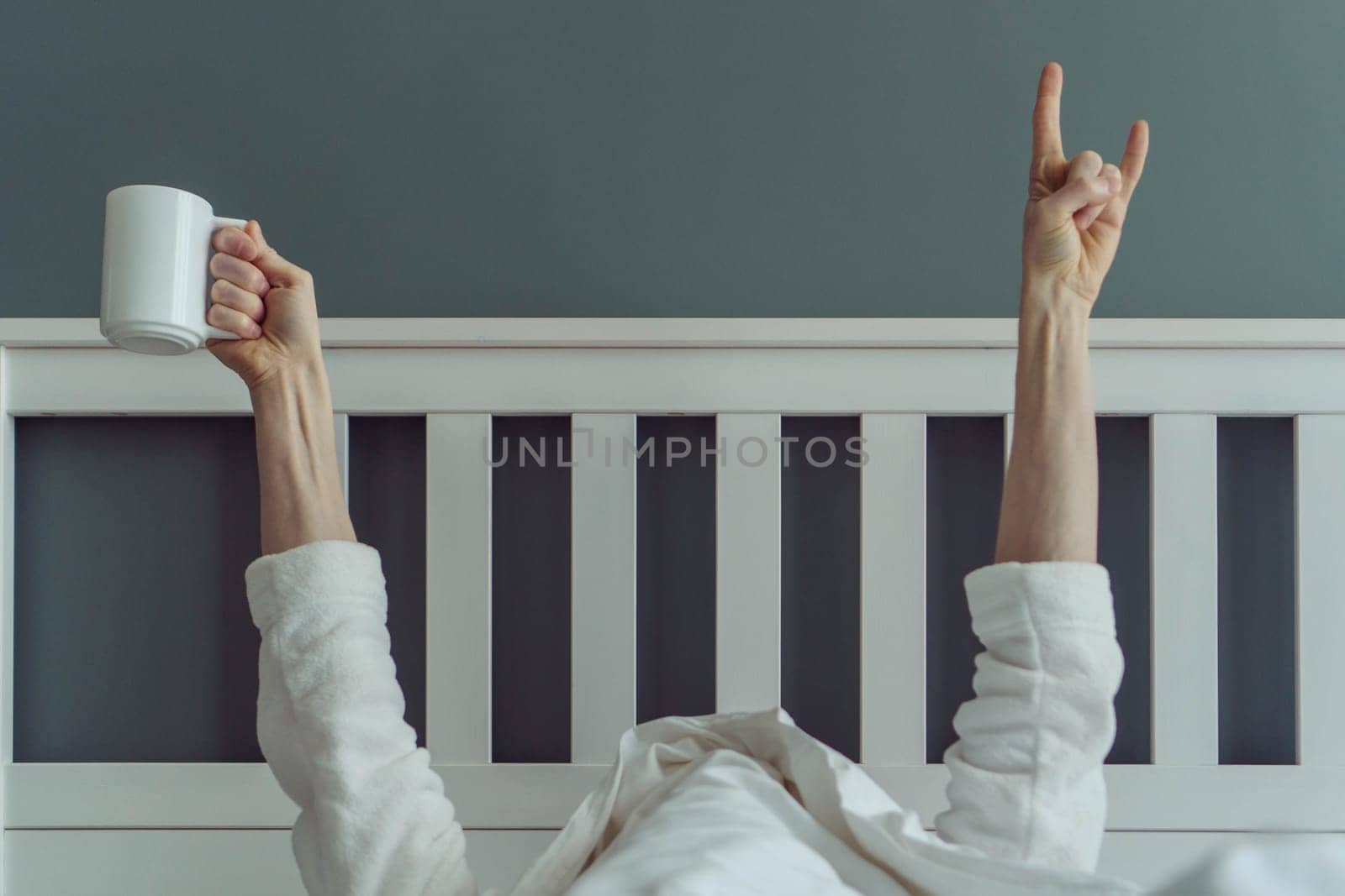 Wonderful start to new day. Unrecognizable man wakes up and stretches in comfortable bed, holding cup of fragrant coffee in his hands. Positive emotions. Have great night's sleep.