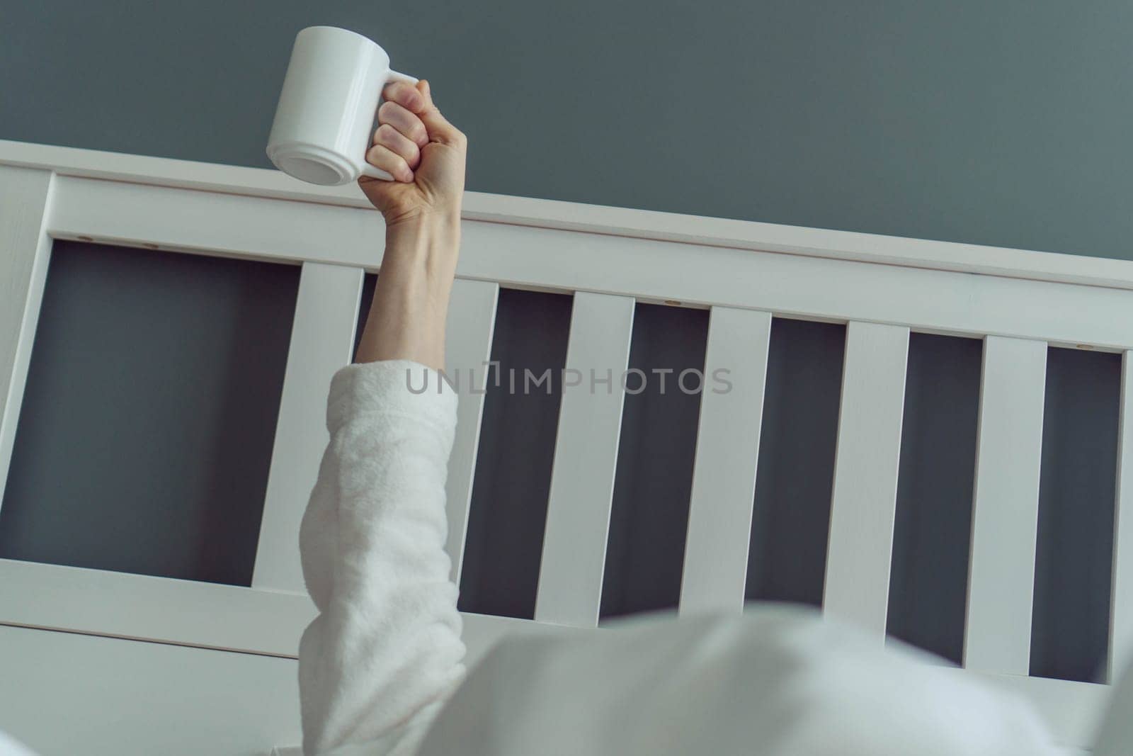 Great mood, first day of vacation. Unrecognizable man wakes up and stretches in comfortable bed, holding cup of fragrant coffee in his hands. Positive emotions. Beginning of day.
