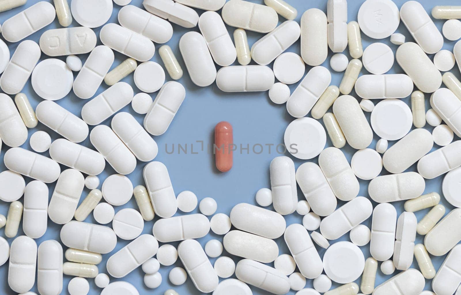 Mix of white medical capsules and pills with one pink capsule in the middle on light blue top view. Medicinal treatment. Taking dietary supplements and vitamins. Assorted pharmaceutical products