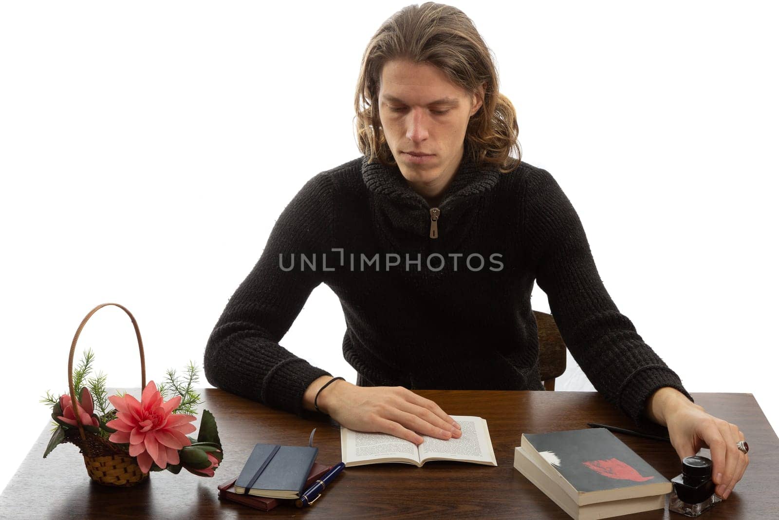 A student sits at a table and reads a book on a white background