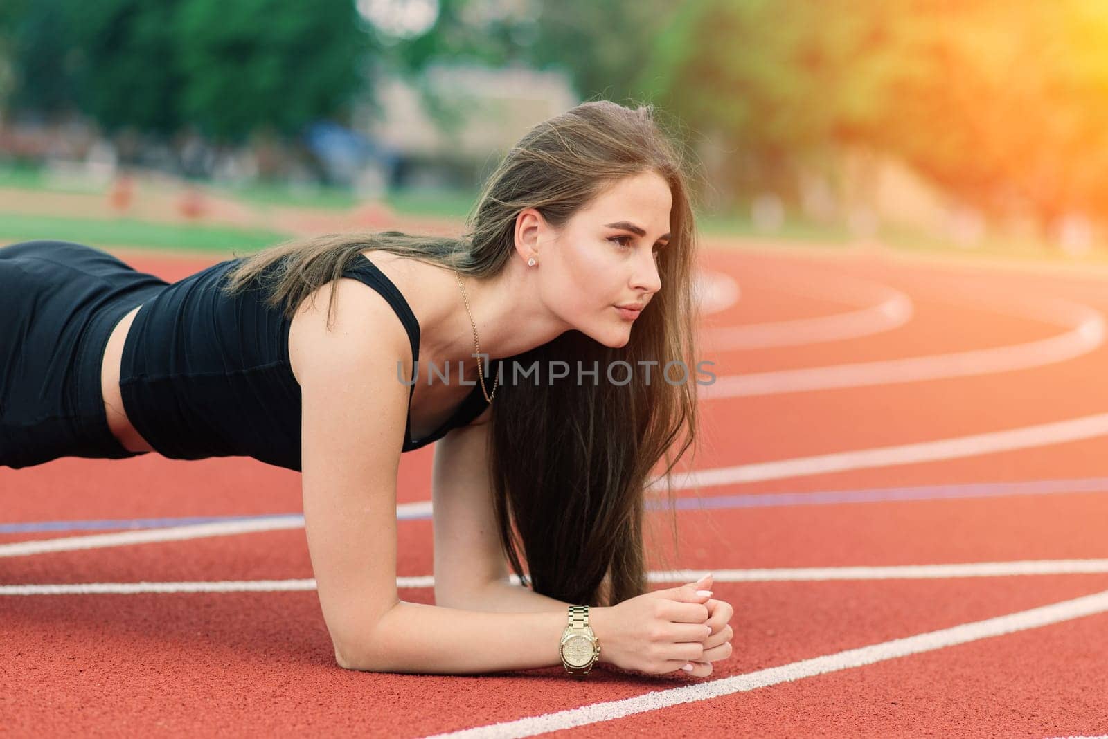 A female coach with dark hair stands on the red running track of the stadium, dressed in sports uniform.