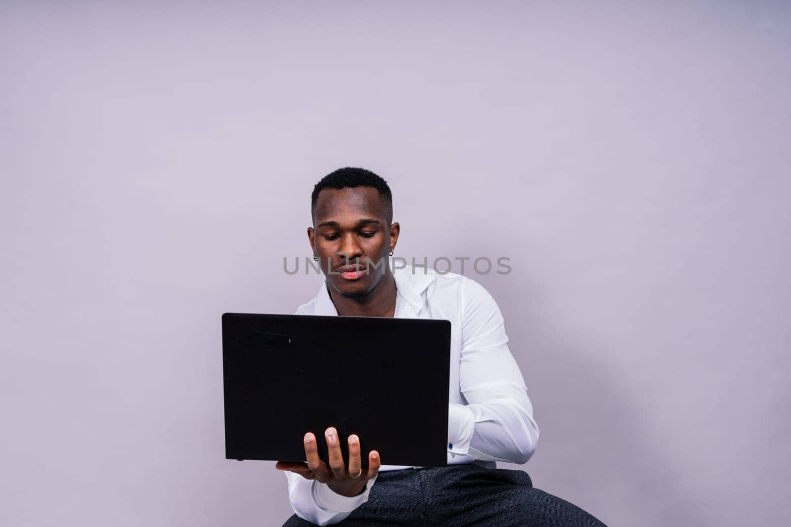 Optimistic african-american male student in a casual shirt using laptop pc isolated