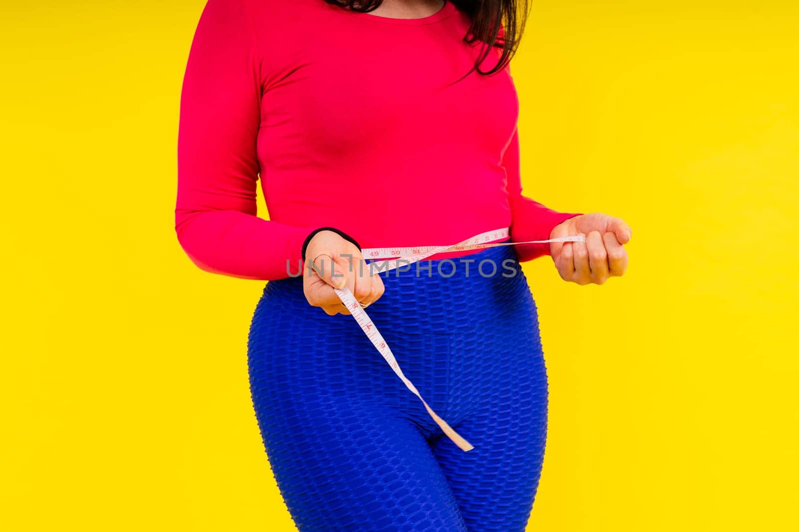 Overweight woman measuring waist before weight loss in a studio shot on yellow background