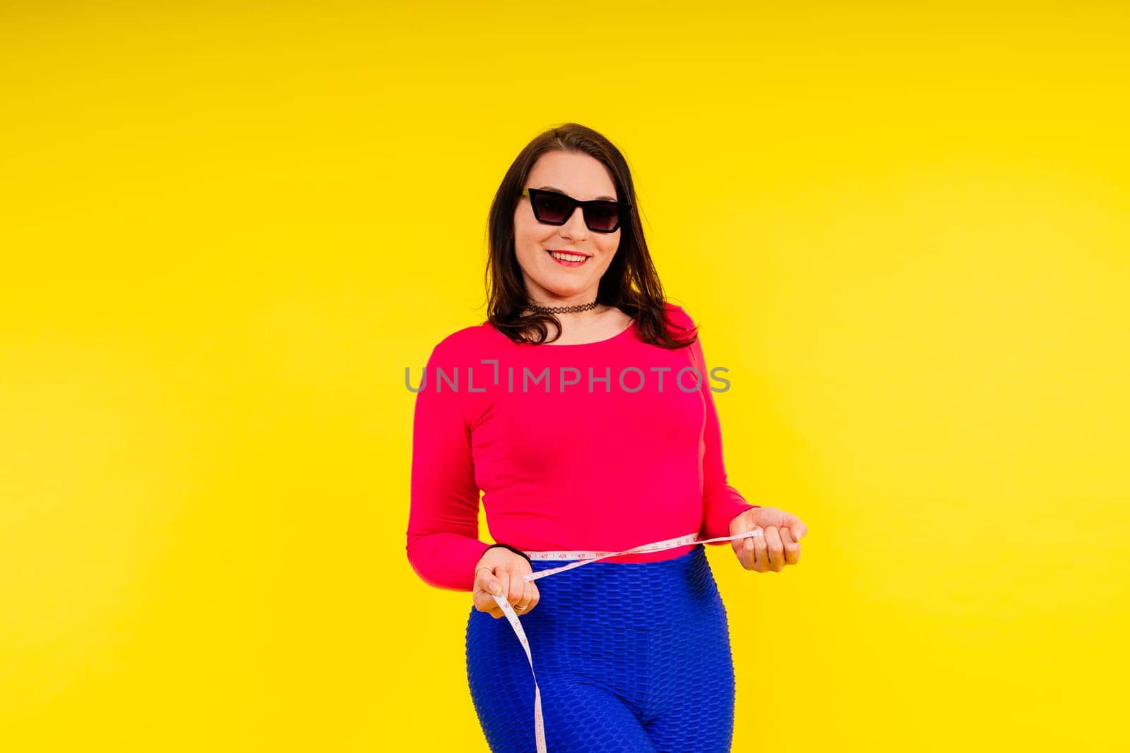 Overweight woman measuring waist before weight loss in a studio shot on yellow background