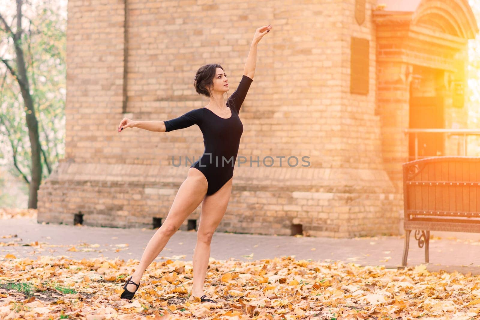 Beautiful female, ballerina, athlete in black bodysuit training in park