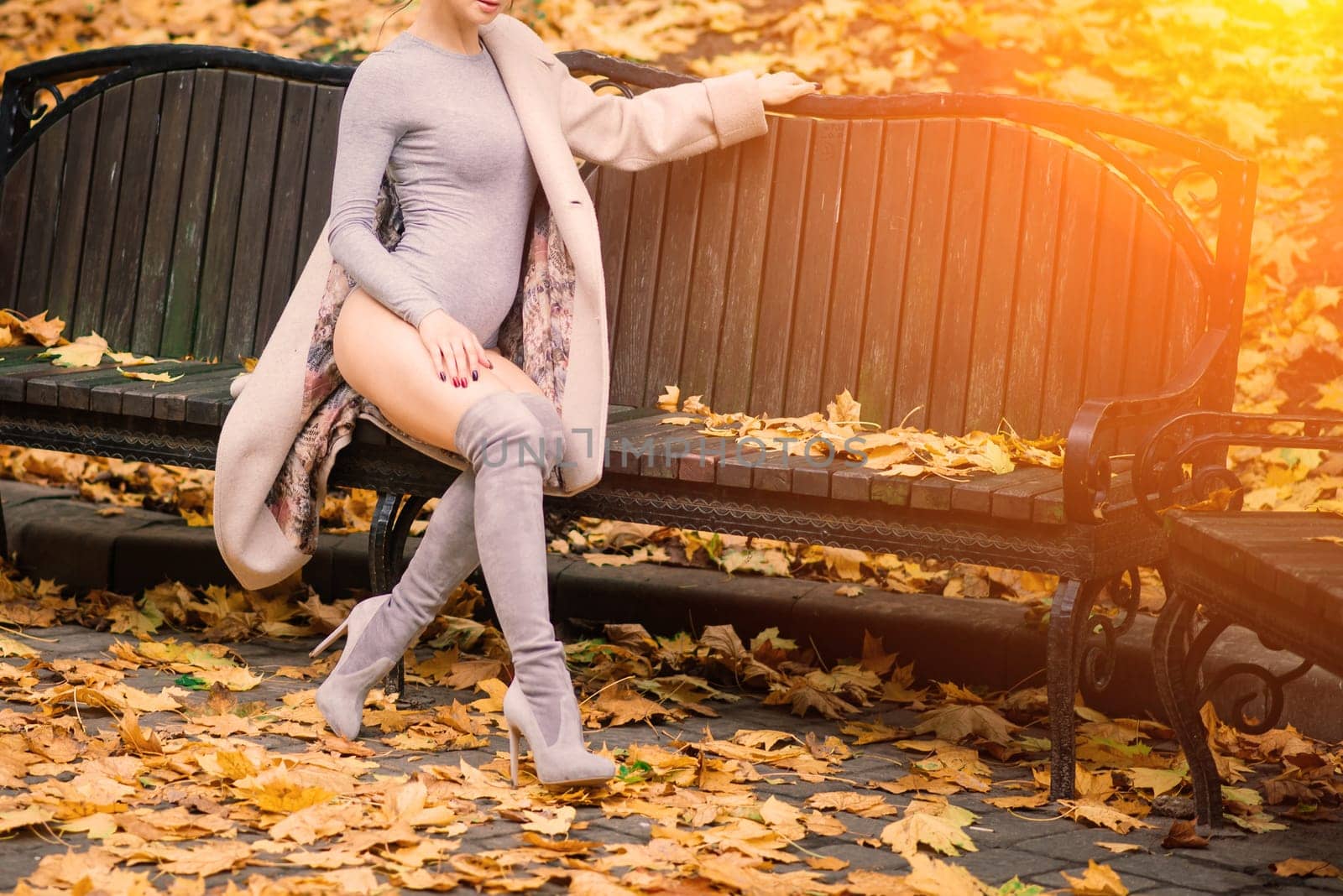 Young beautiful dark-haired woman with a slender figure posing in lingerie and a classic coat in an autumn park