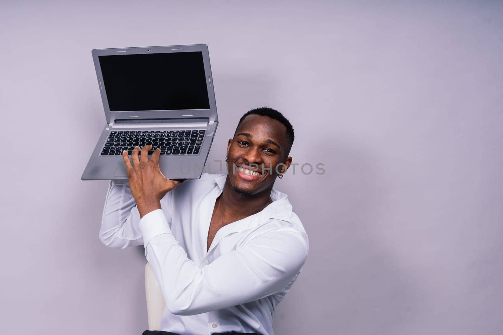 Optimistic african-american male student in a casual shirt using laptop pc isolated
