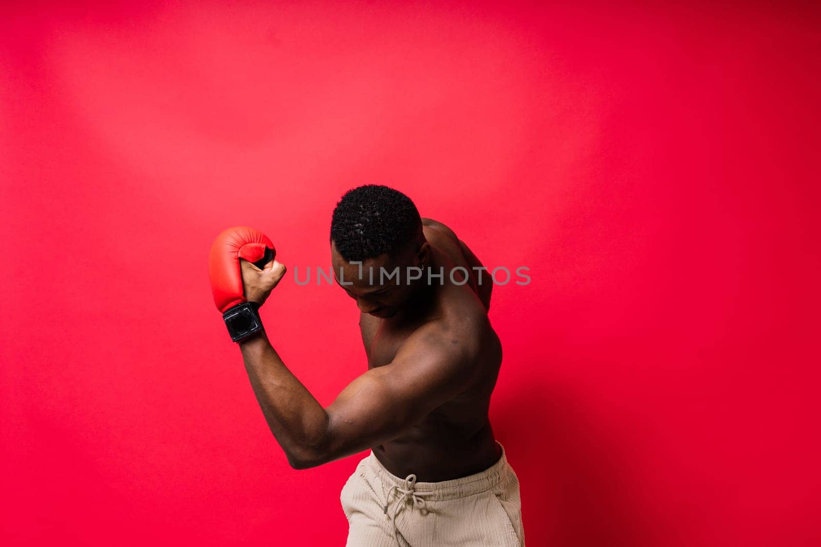 Muscular serious looking african boxer training, in studio red background