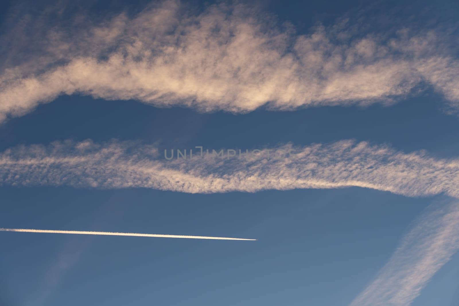 Landscape of a beautiful blue sky with clouds, white vapor trails and a plane in the evening. Nature.