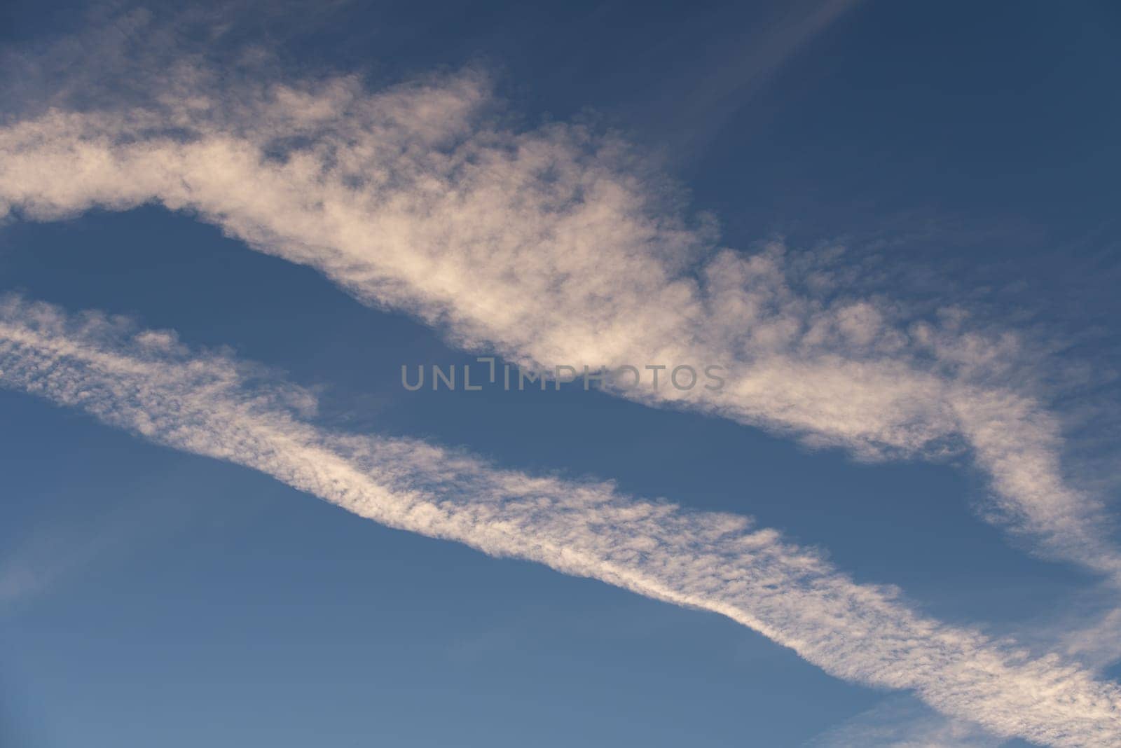 Landscape of a beautiful blue sky with clouds and white vapor trails in the evening. Nature.
