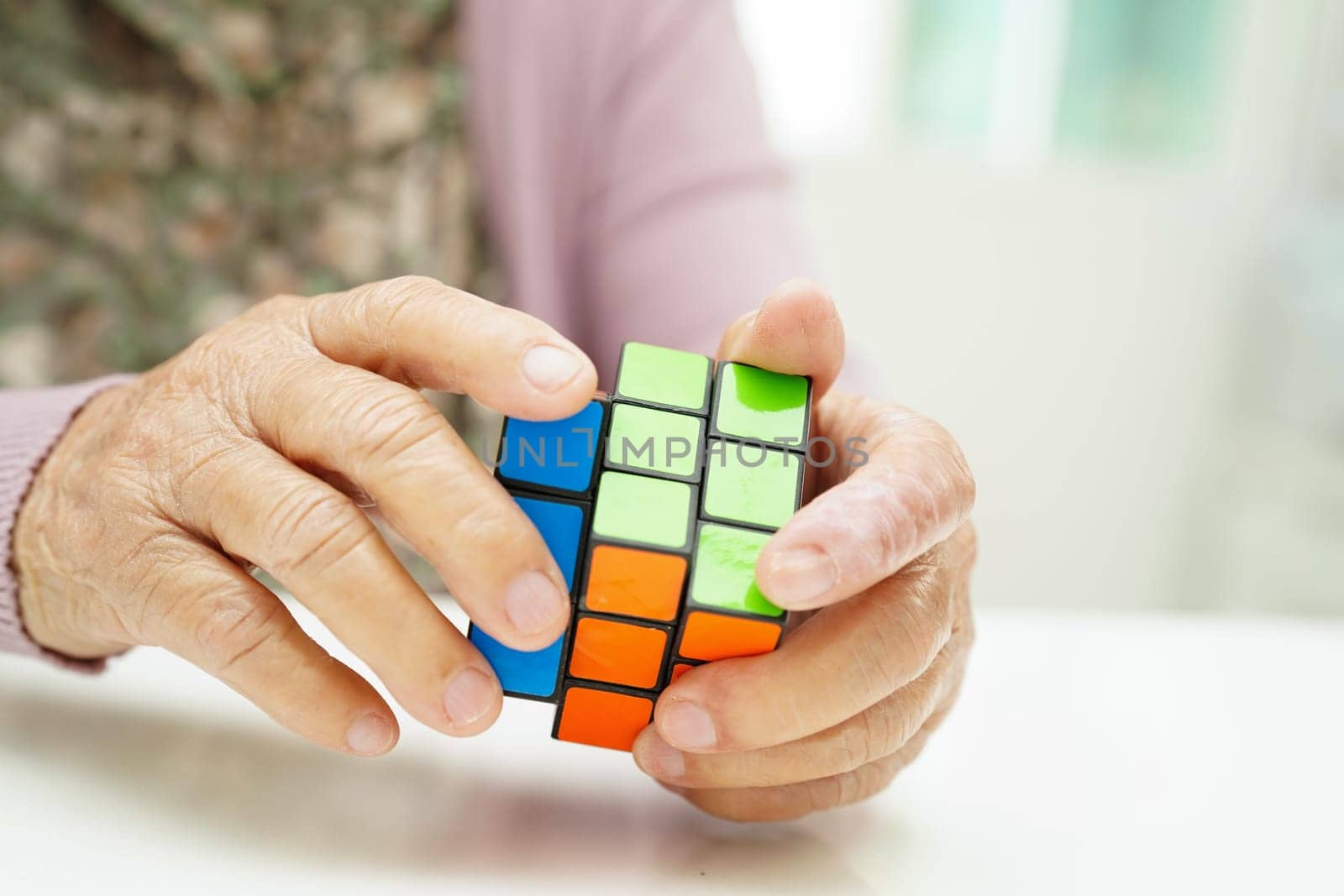 Bangkok, Thailand - May 15, 2022 Asian elderly woman playing Rubik cube game to practice brain training for help dementia prevention and Alzheimer disease.