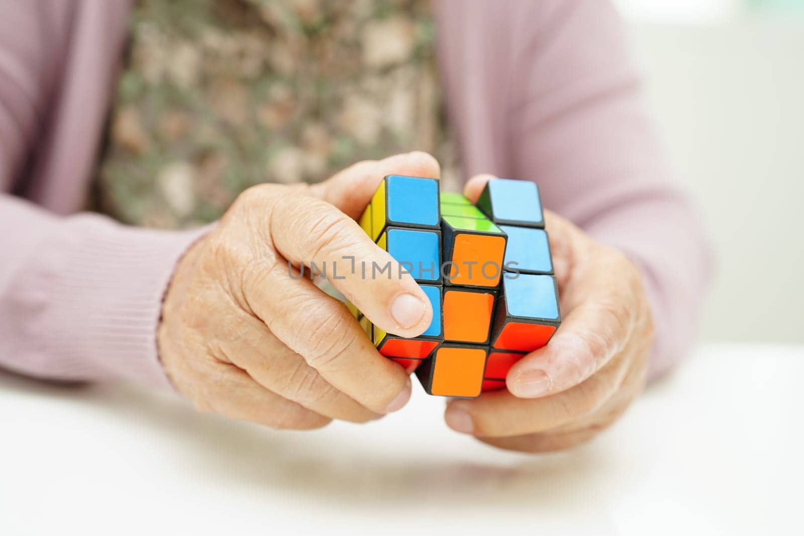 Bangkok, Thailand - May 15, 2022 Asian elderly woman playing Rubik cube game to practice brain training for help dementia prevention and Alzheimer disease.
