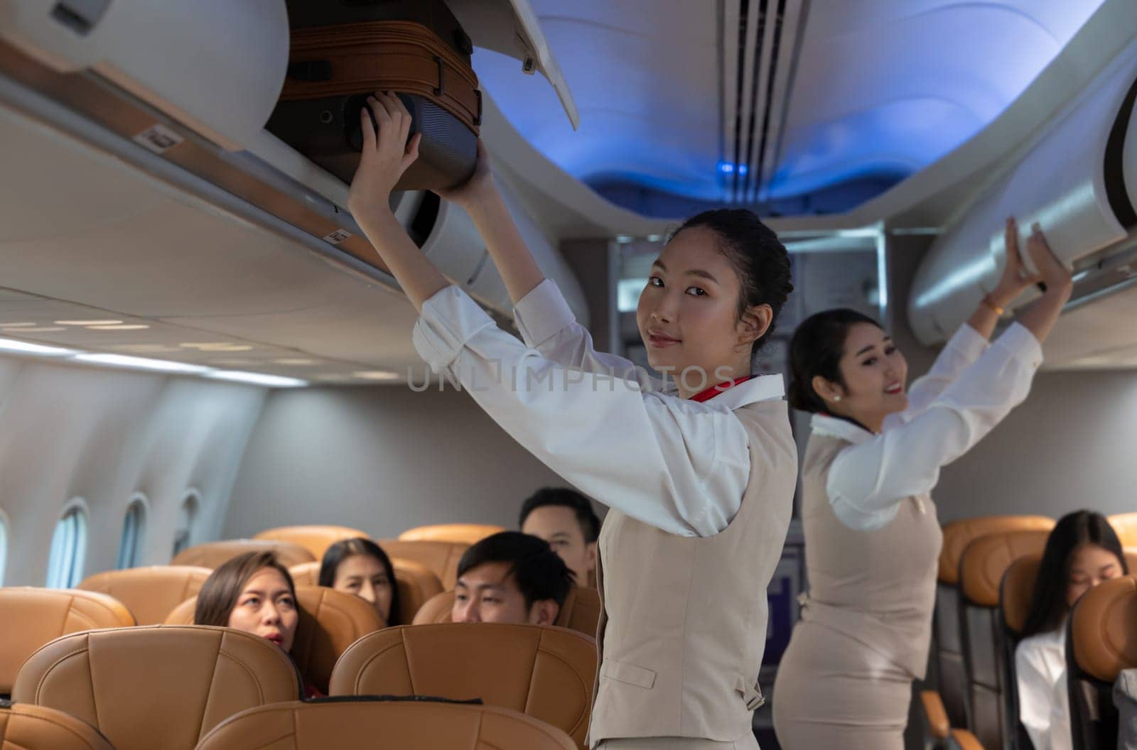 Air hostess or cabin crew working in airplane. Female flight attendant putting luggage and closing cabin compartment. Airline transportation and tourism concept.