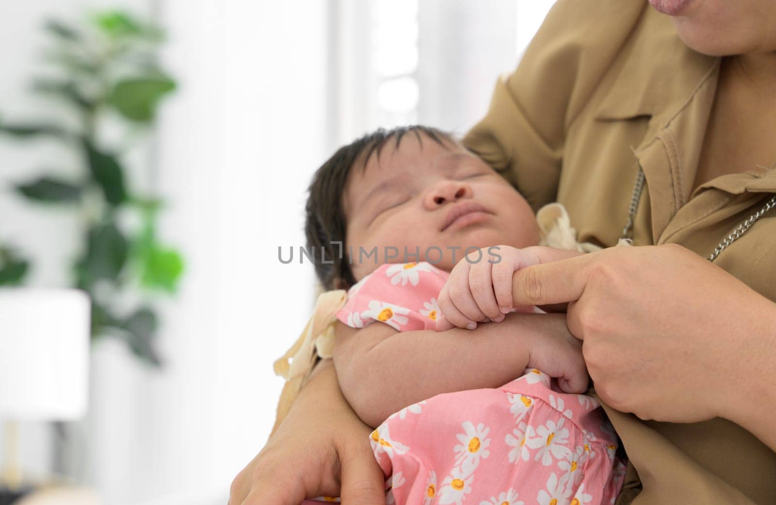 Cute healthy newborn baby girl or boy 1 month sleeping on mother arm and holding her mom finger in bedroom at home. Care, love and mothers day concept.