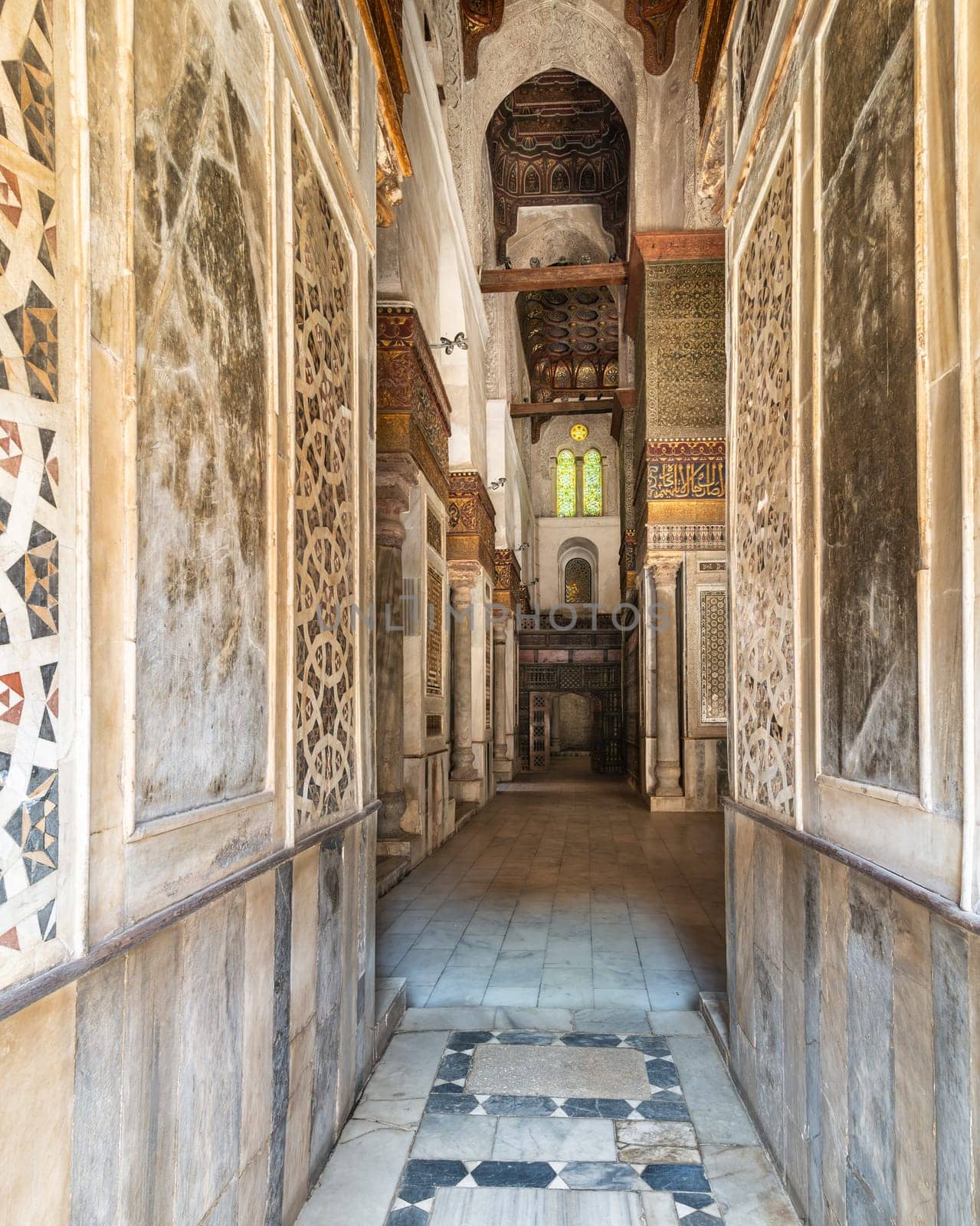 Narrow hallway with decorated marble walls in the Qalawun Complex, a historic Islamic complex located on Moez Street in Cairo, Egypt. The corridor features a beautiful stained glass window at one end