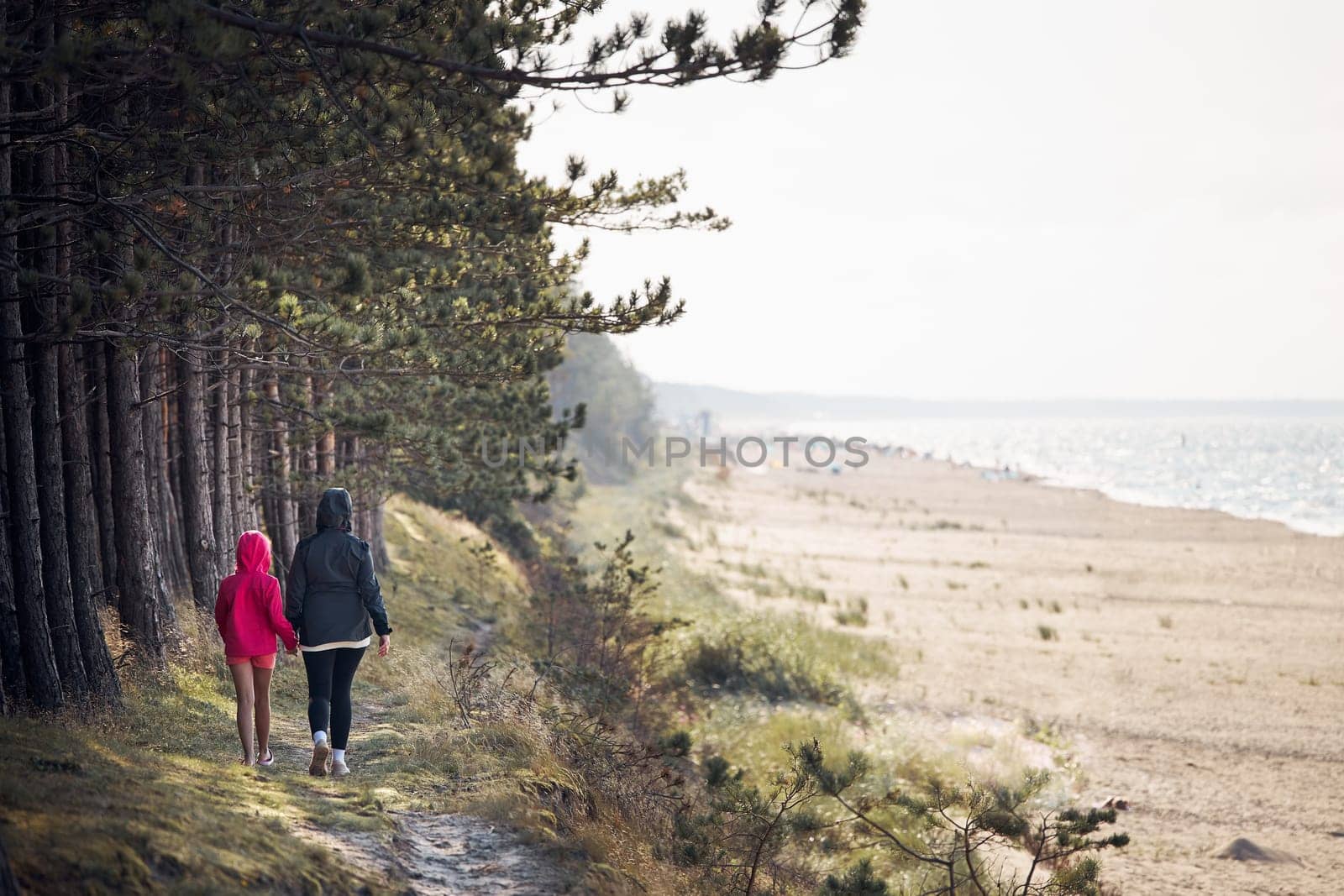Family walking in forest along beach. Summer vacation trip close to nature. People actively spending leisure time. Back view of woman with daughter enjoying long walk during summertime. Travel concept