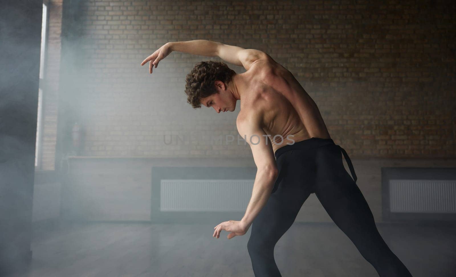 Graceful athletic ballet male dancer demonstrating strong perfect upper body. Shirtless muscular man dance performer view from back