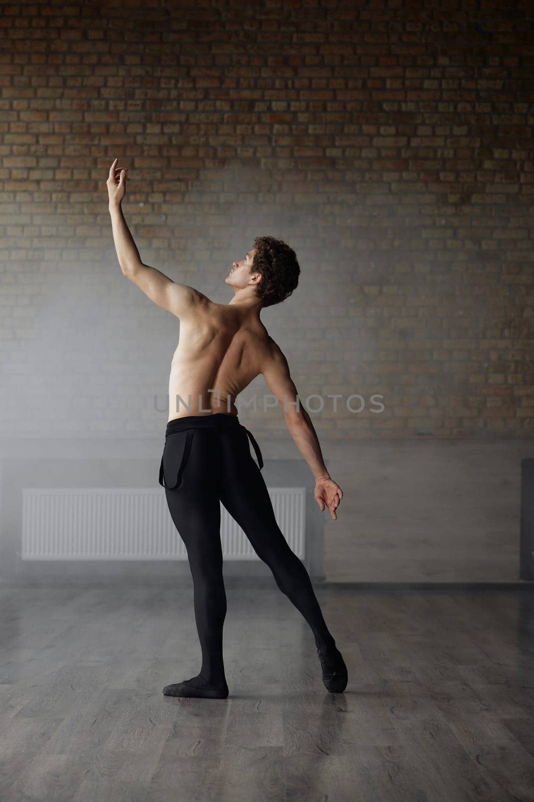Handsome shirtless man ballet dancer making dance element against studio background. Modern choreographer training indoors