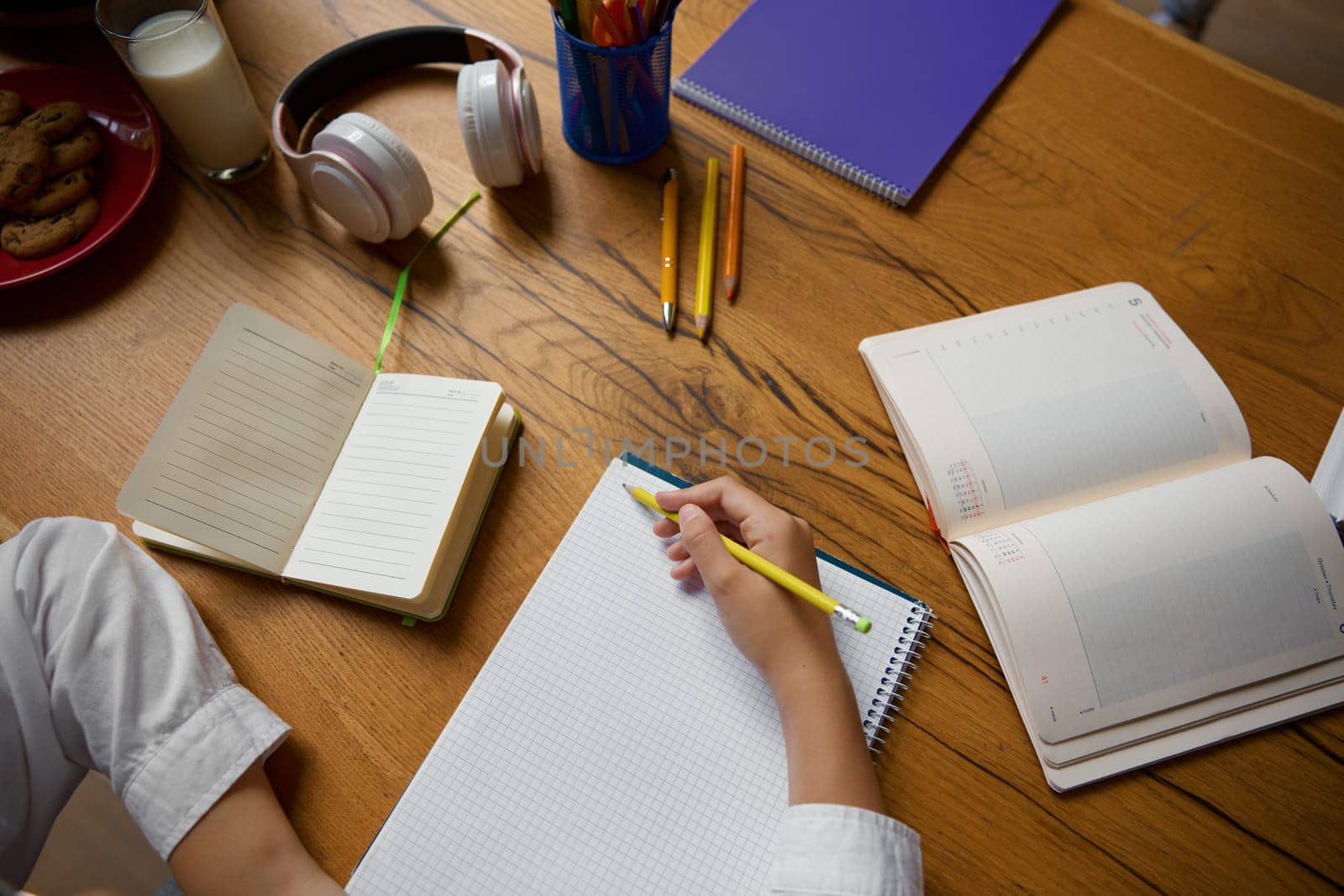 High angle view closeup on little student hands writing in copybook. Elementary school child doing homework learning at home