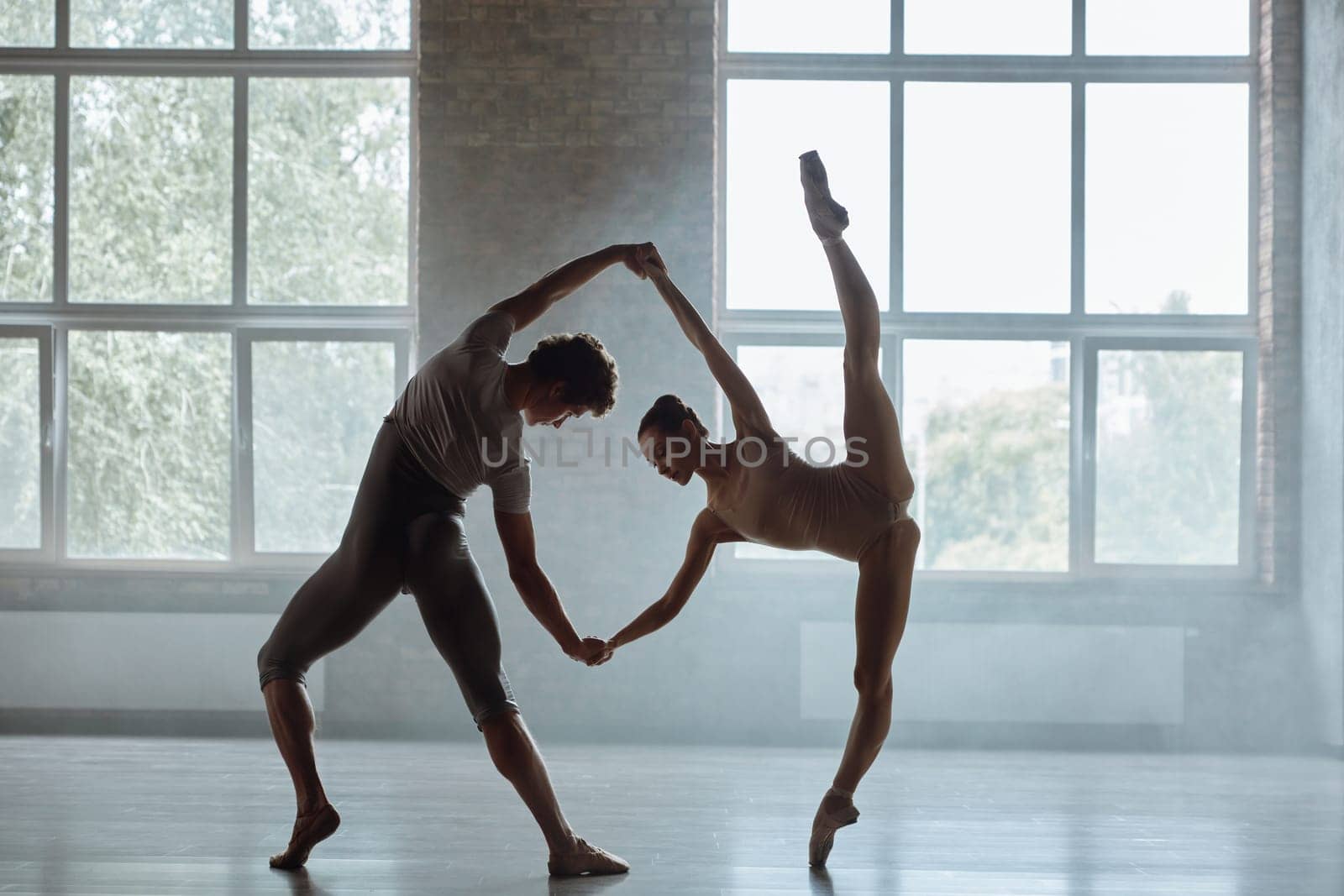 Silhouette of man and woman ballet dancers performing together against studio background. Contemporary choreography performance