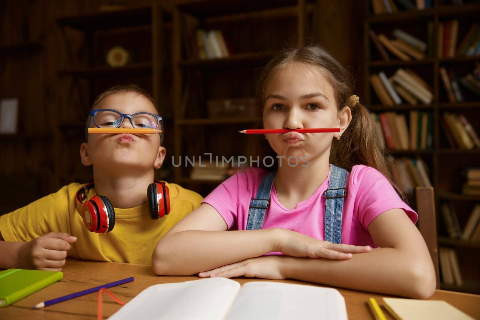 Portrait of cute children holding pencil on mouth under nose. Mischief humor boy and girl siblings feeling playful and fooling around. Happy childhood and interesting home education