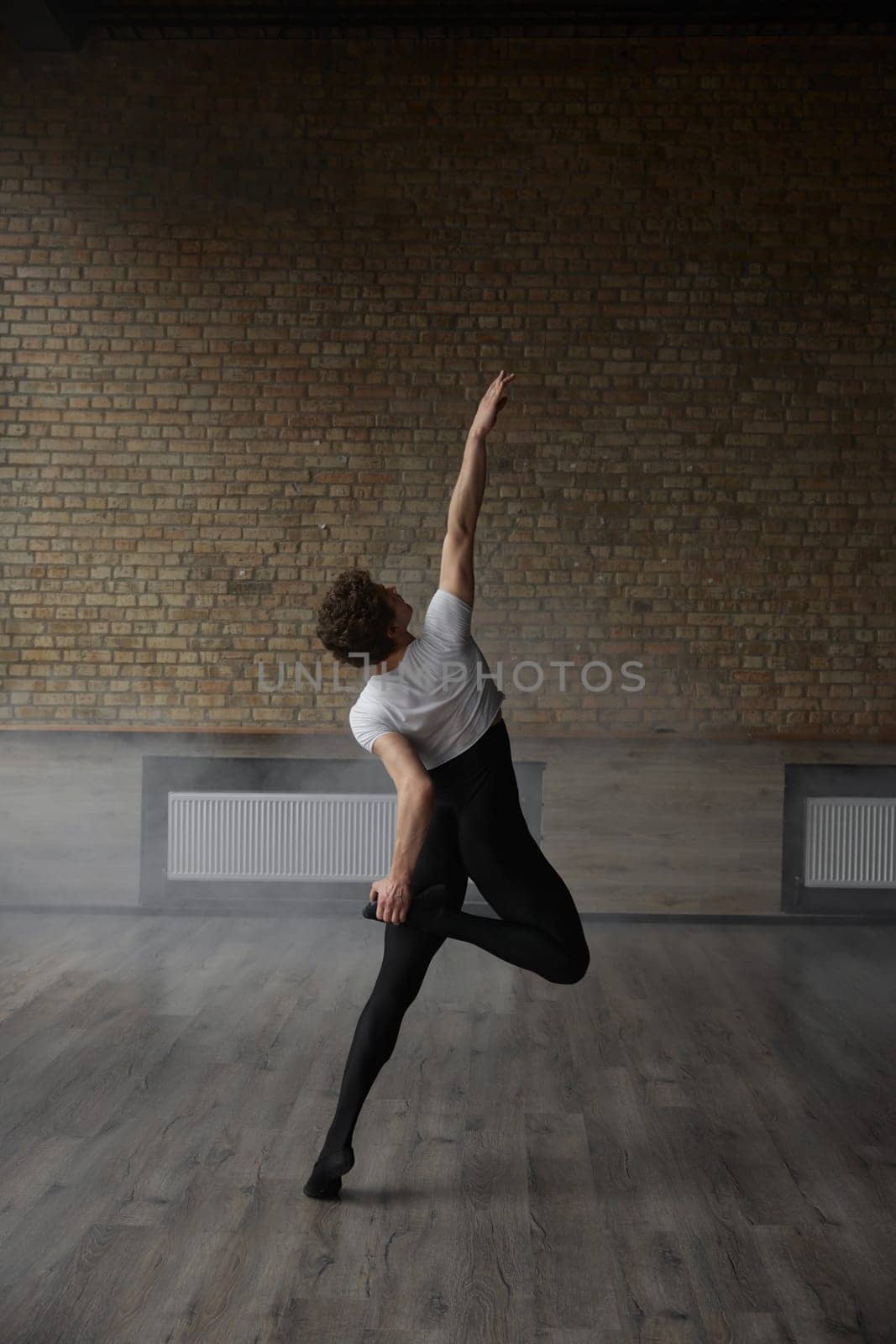 Contemporary ballet male dancer posing for camera performing body stretching routine. Modern dancing studio