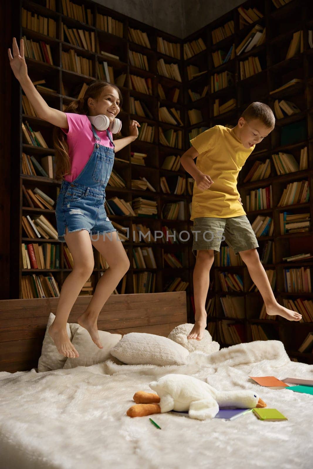 Crazy little sister and brother jumping in bed after successful remote school class. Active children and online education