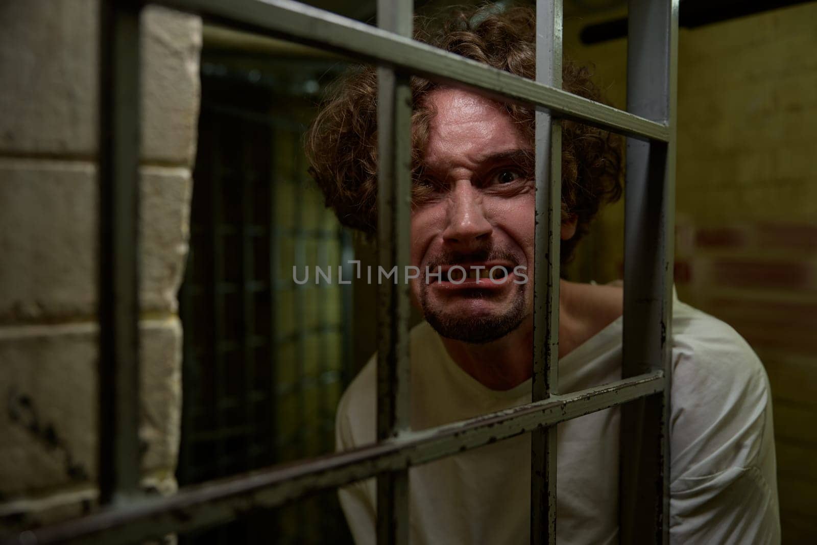 Portrait of caged crazy man with mad face crying bitterly and suffering from mental disorder