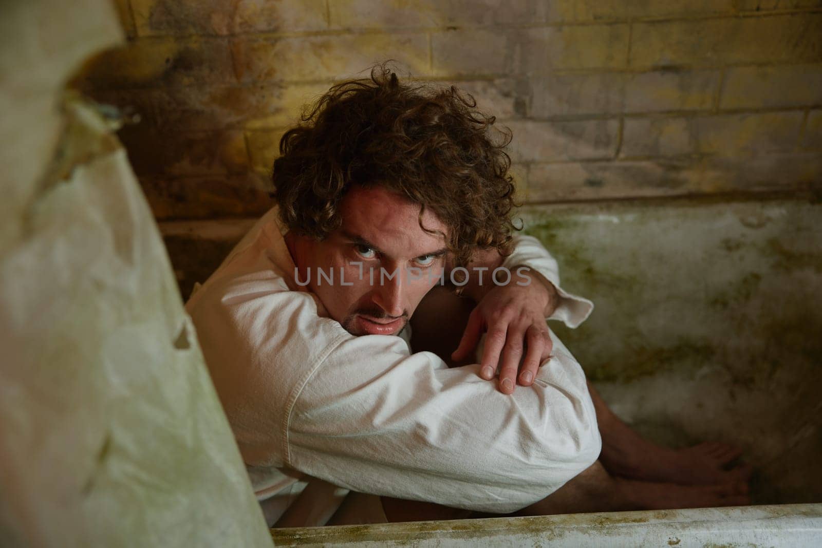 Crazy man hiding in dirty bathtub feeling scared suffering from schizophrenia and attack of horror with panic