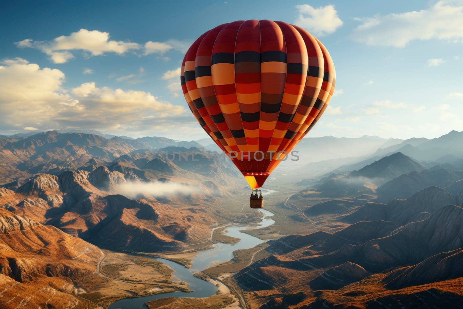 Red orange hot air balloon flies against a partly cloudy sky above a river through a beautiful valley with a backdrop of mountains