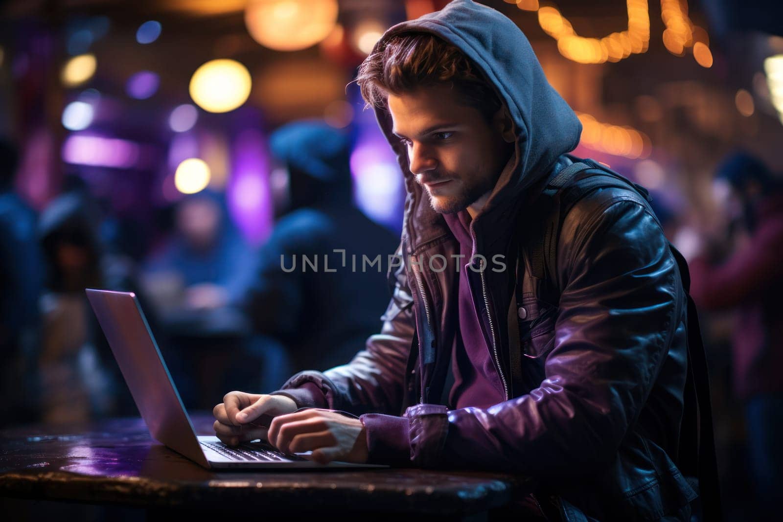 Young man working on laptop, male freelancer or student with computer in cafe with neon lighting at table, looking at camera.