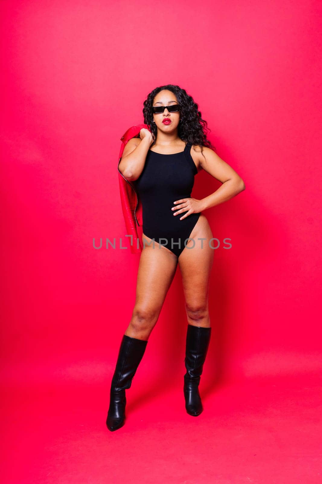 African American curvy female in black bodysuit and jacket on red and white background in a studio