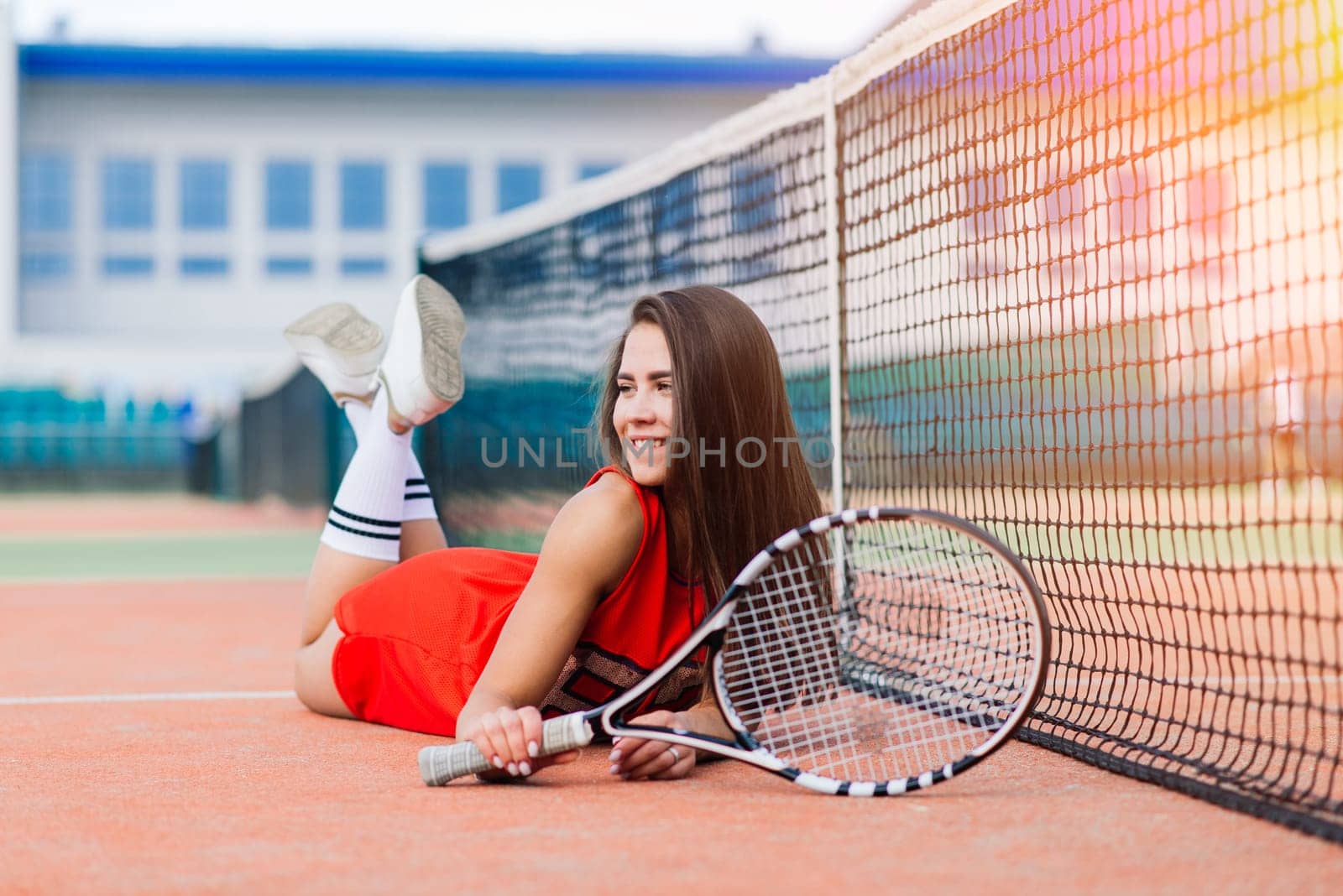 Beautiful female tennis player on tennis court in red dress.