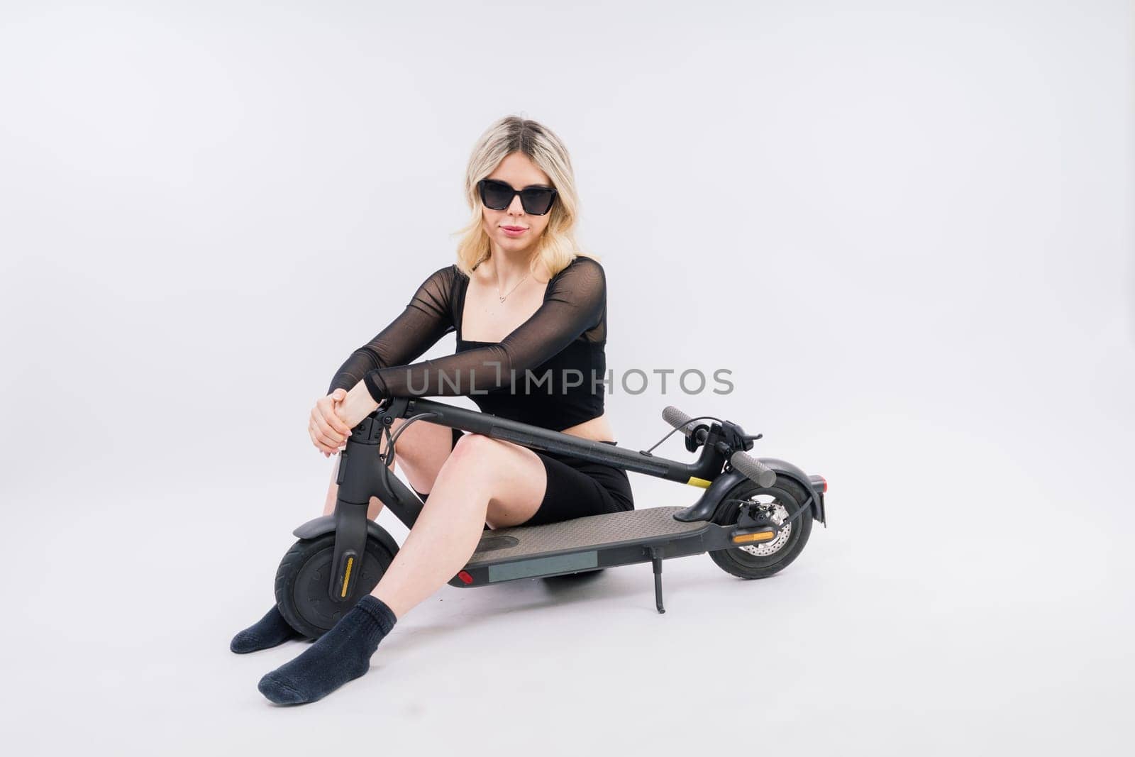 Blonde woman on a red and white background sit and stand with electro scooter and resting