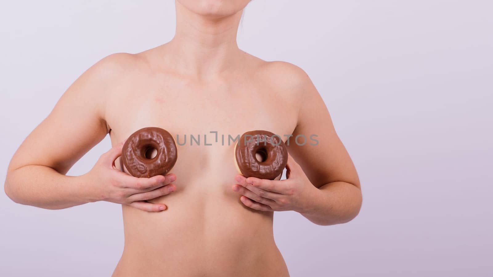 Close up shot of nude topless woman holding chocolate covered donuts