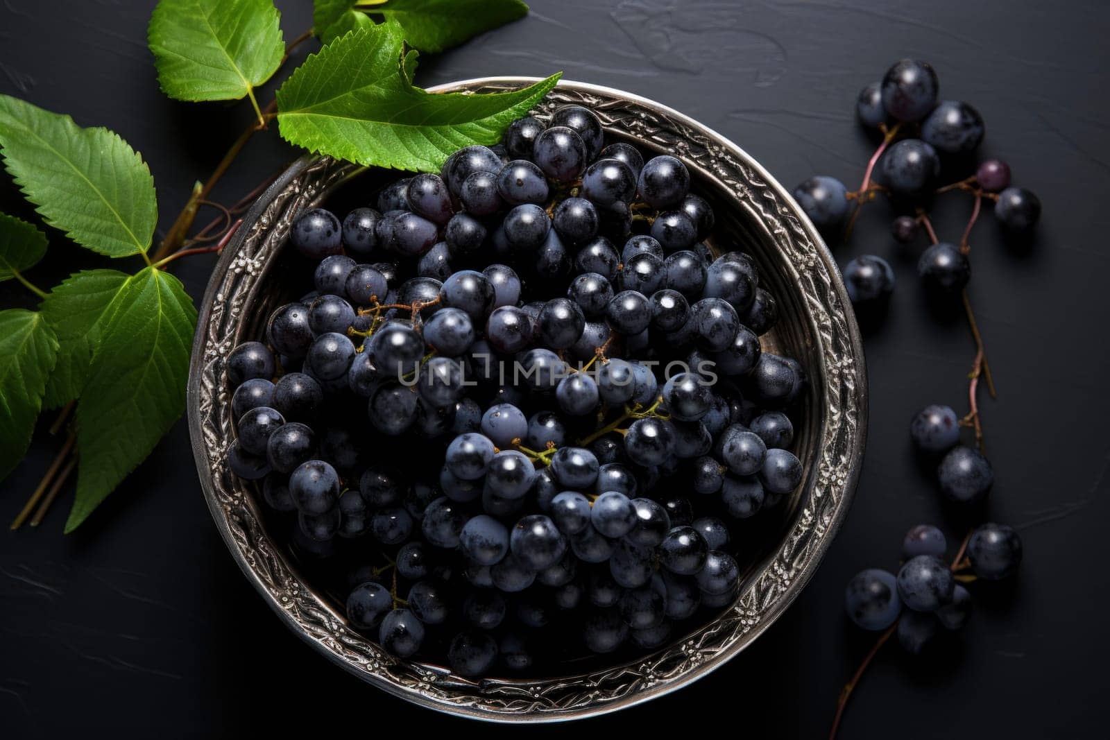 Black grapes in plate with vine plant on dark table top view. Sweet juicy grapes food on black concrete background