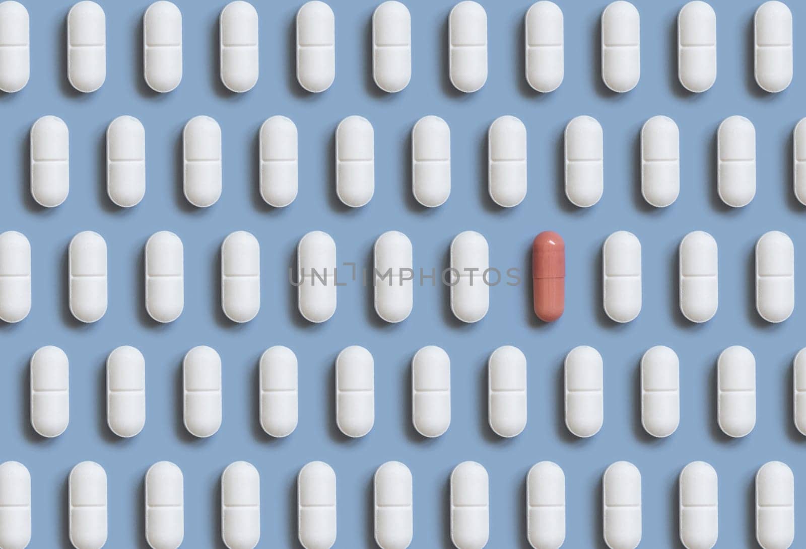 Mix of white medical pills in a line with one pink capsule on light blue top view. Preventive medicine and healthcare, dietary supplements and vitamins. Assorted pharmaceutical medicine capsules