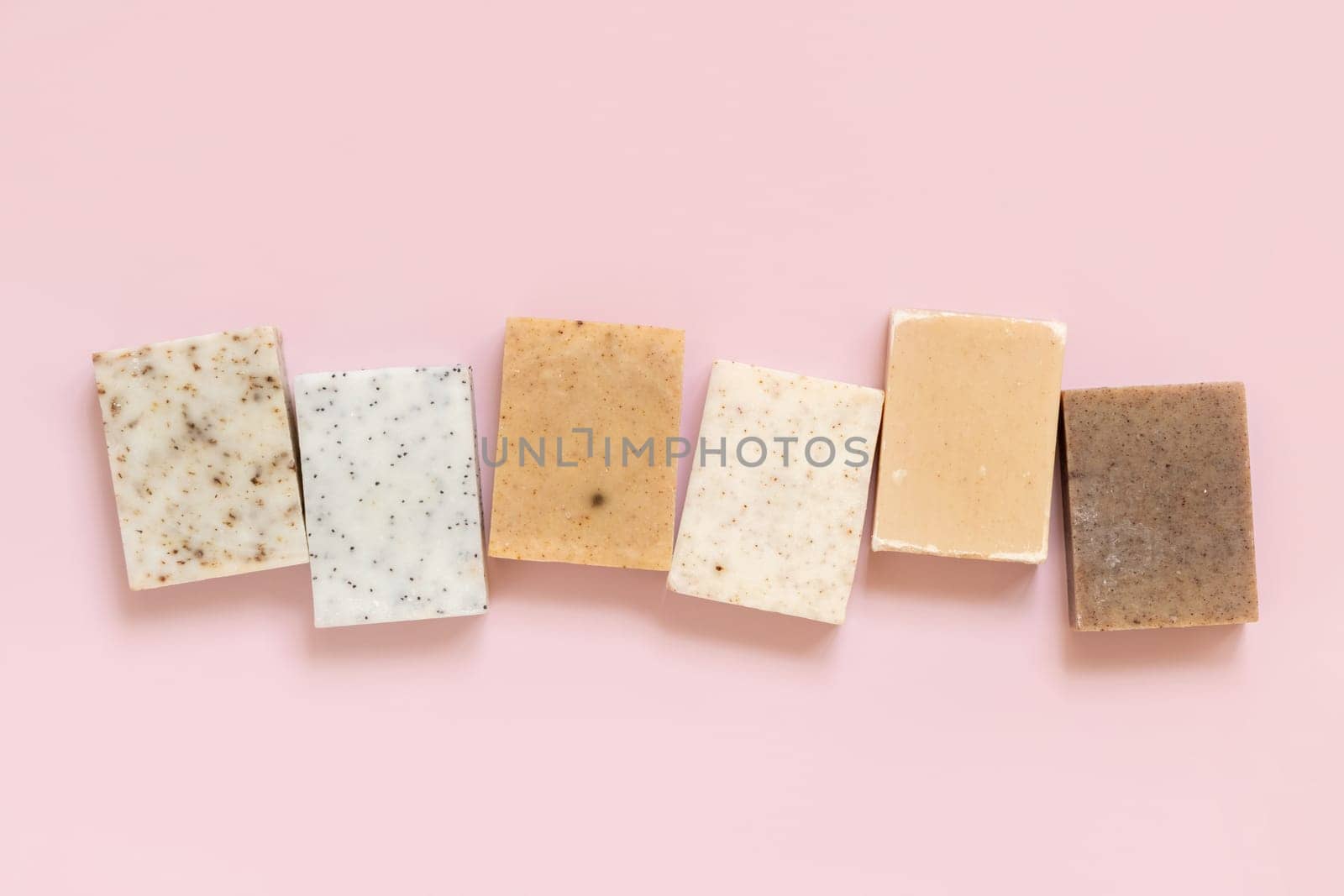 Beige and brown handmade soap bars in a line on light pink top view, copy space. Natural herbal products for Spa and skin care. Using organic handmade skincare products in everyday routine