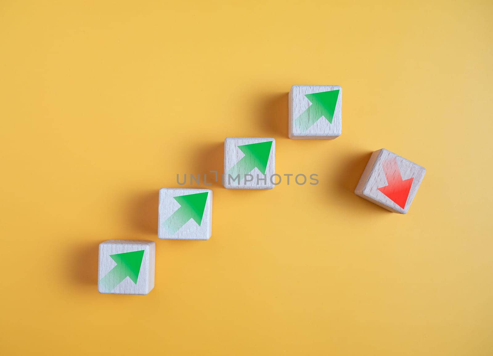 Green arrow and red arrow on wooden block represents economy trending downwards on yellow background. Economy recession crisis, inflation, stagflation, business and financial loss concept.
