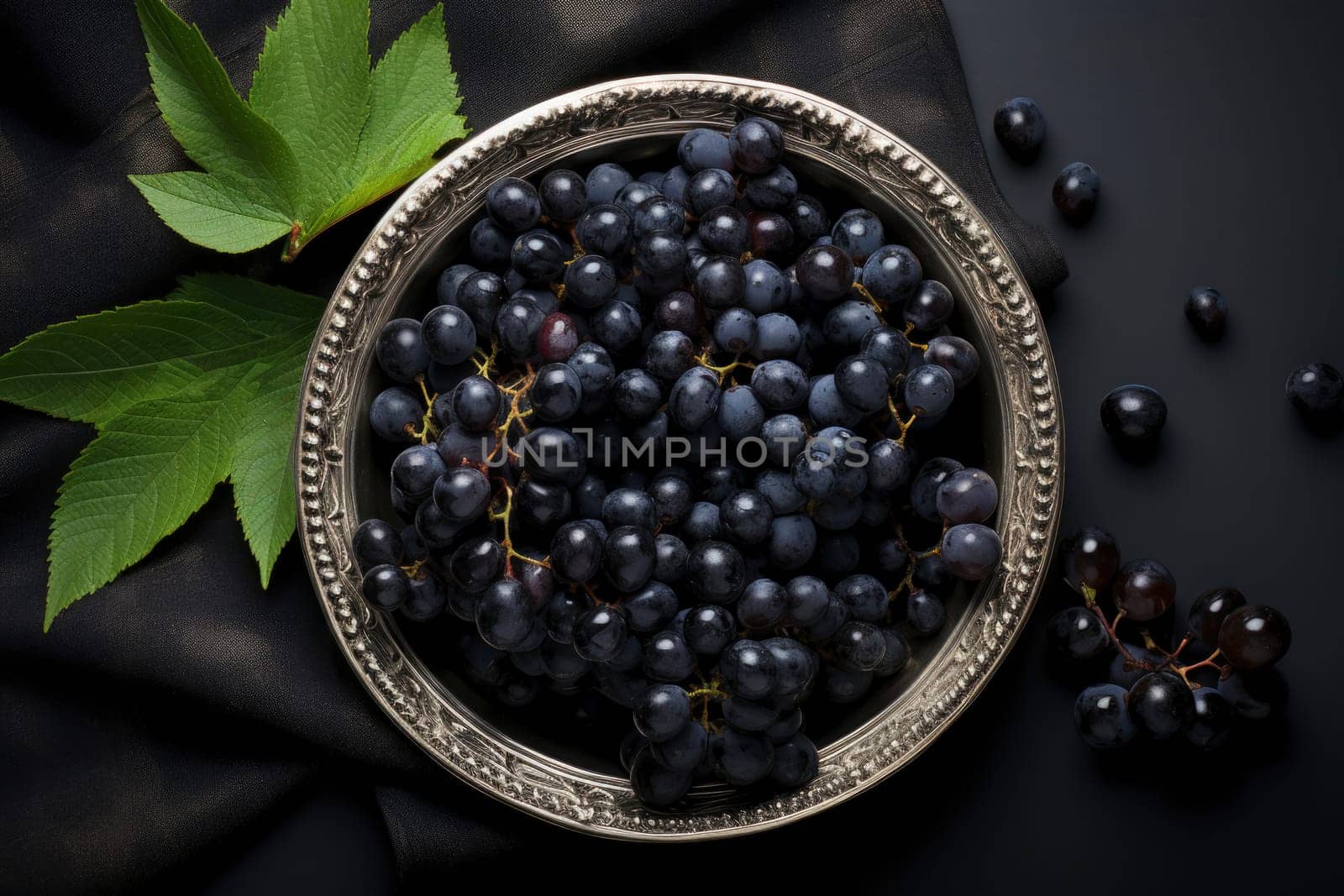 Black grapes in plate with vine plant on dark table top view. Sweet juicy grapes food on black concrete background