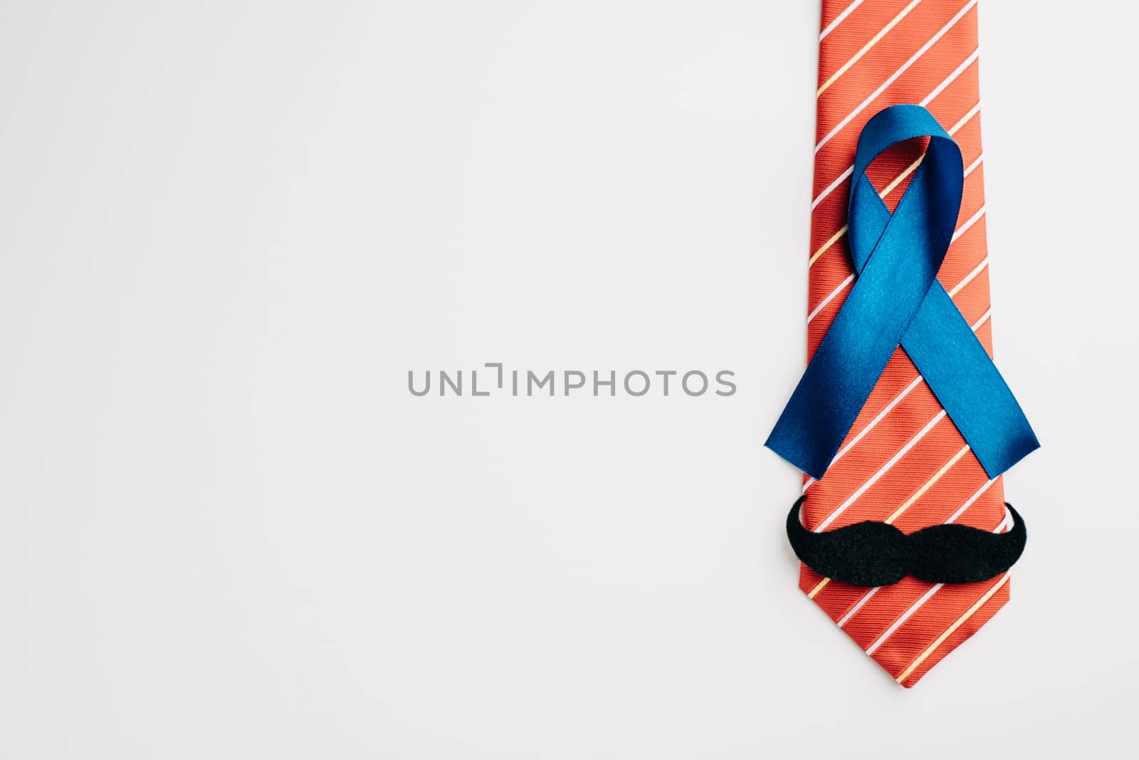A blue ribbon adorned with a mustache and necktie, symbolizing Prostate Cancer Awareness, signifies support for those affected by the illness. Men's healthcare and World Cancer Day concept.