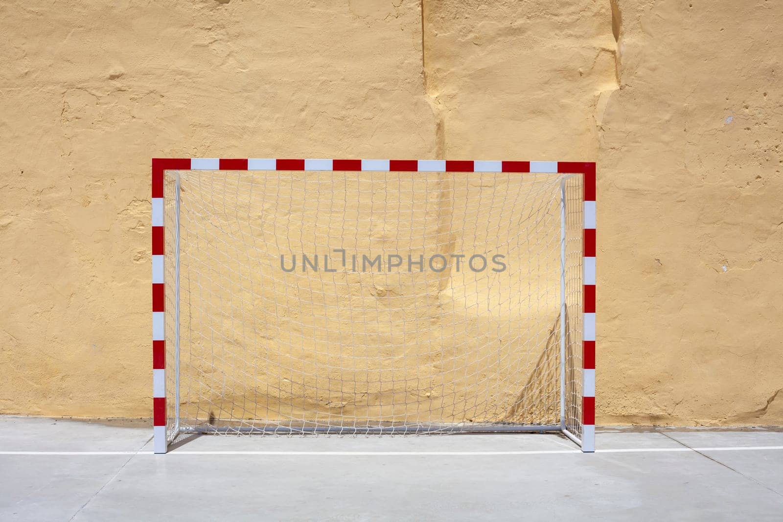 Soccer ball and goal with net against plastered wall background. Football at school yard scenery